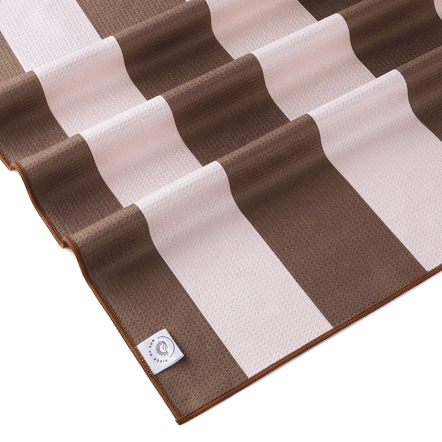 Close-up van het beige-witte gestreepte strandlaken van Piece of Sun. Gemaakt van luxe microvezel met wafelstructuur, ultrazacht, sneldrogend en duurzaam door 85% gerecycled materiaal.