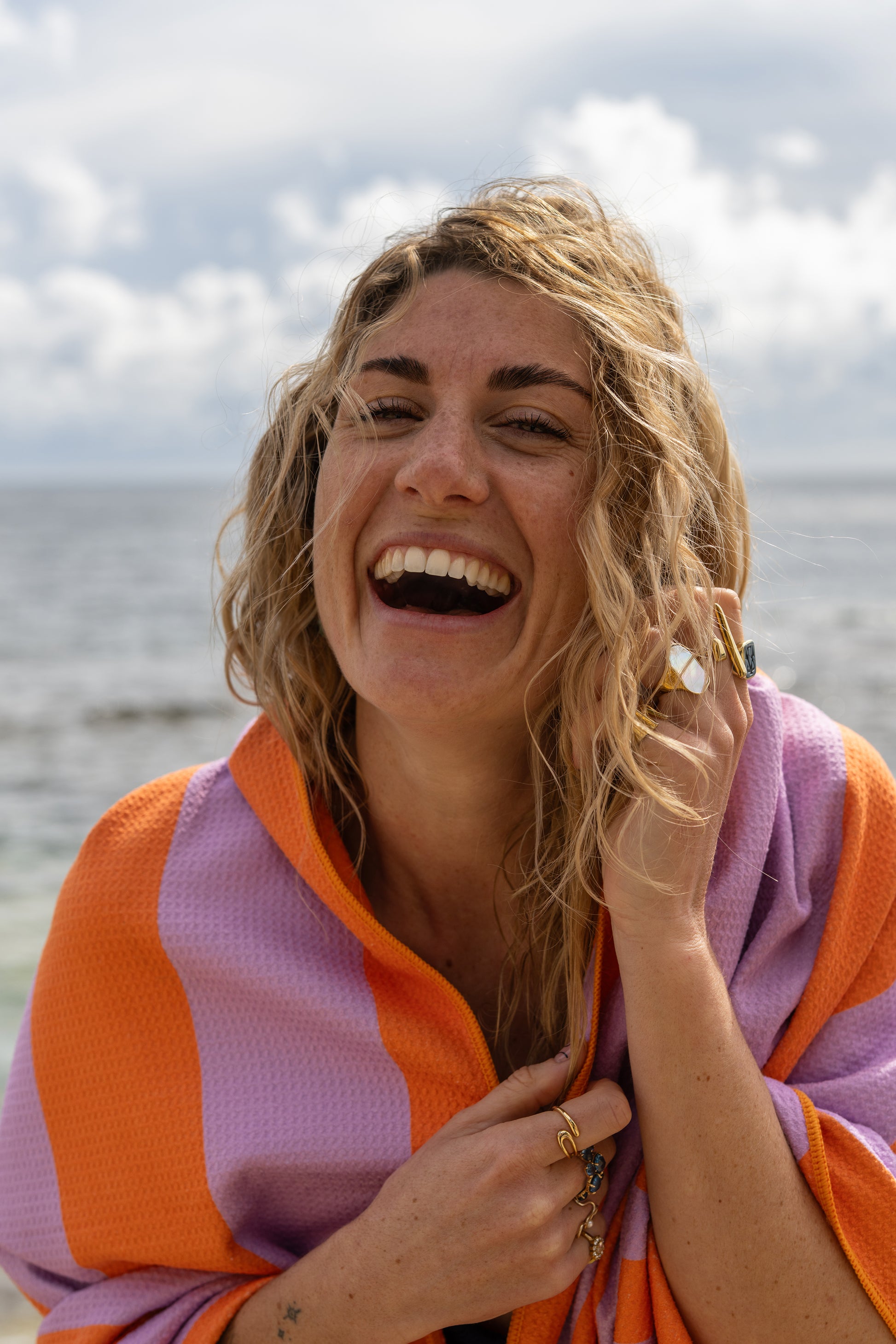 Close-up van een lachende vrouw gewikkeld in het lila-oranje strandlaken van Piece of Sun. Het lichte microvezel met wafelstructuur voelt zacht aan en is gemaakt van 85% gerecycled materiaal.