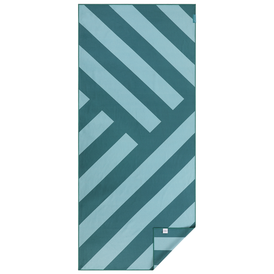 Groot microvezel strandlaken van Piece of Sun met diagonale strepen in turquoise en petrol. Duurzaam geproduceerd van 85% gerecycled materiaal, extra zacht, sneldrogend en ideaal voor strand, spa of vakantie.
