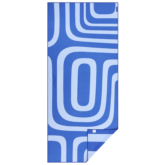 Dubbelzijdige Piece of Sun beach towel met geometrisch retro patroon in blauw en lichtblauw – stijlvol, compact opvouwbaar en ideaal voor strand en reis.